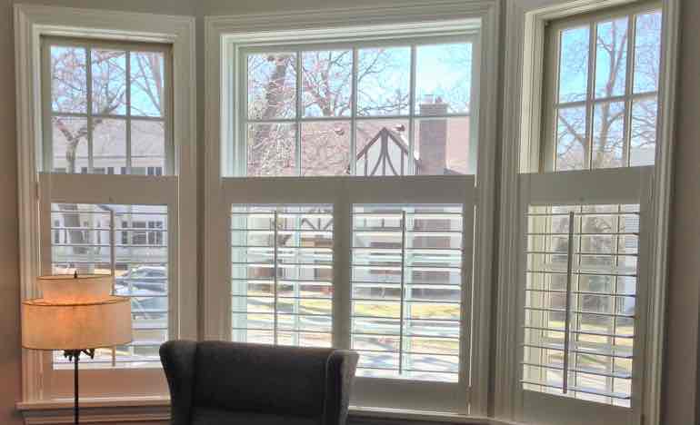 Half-length white shutters in living room bay window.